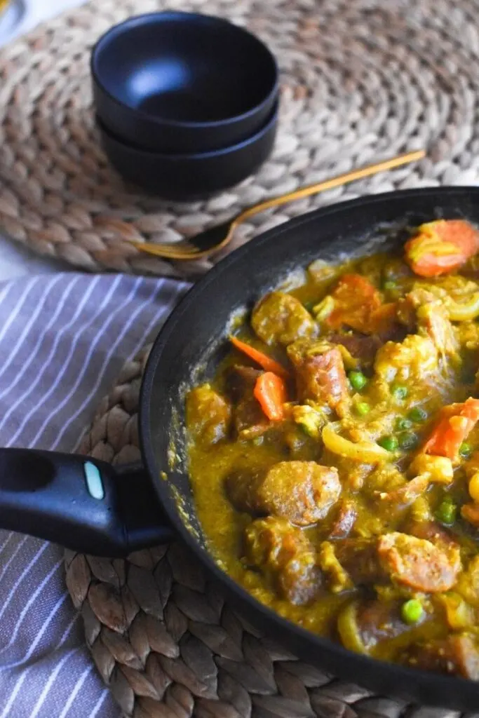curried sausages in frying pan on table