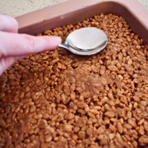 pressing mars bar slice into tin with a spoon