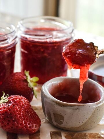 strawberry jam in dish with jar of jam in background.