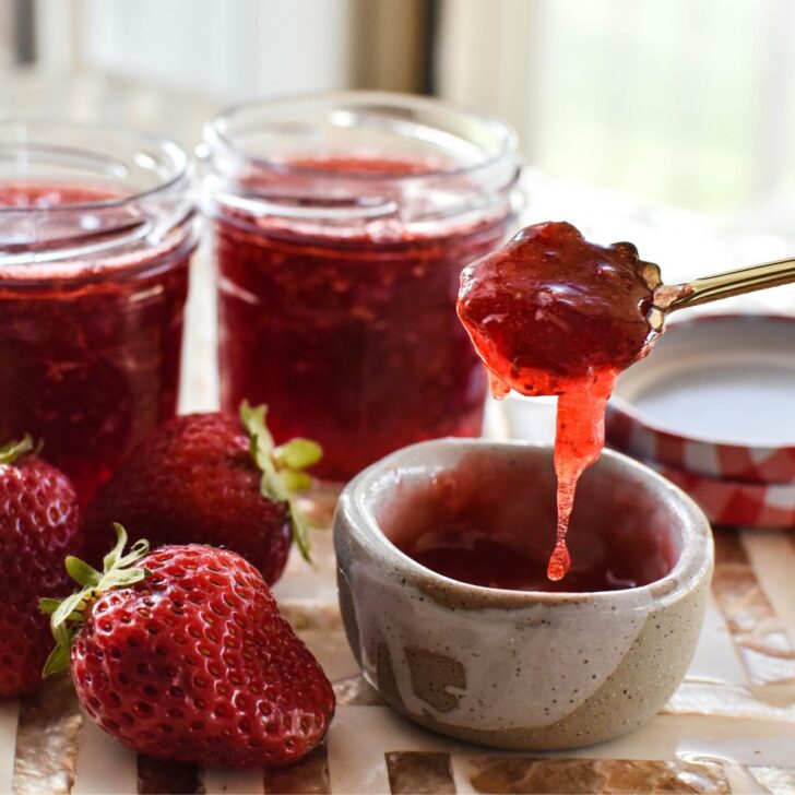 strawberry jam in dish with jar of jam in background.