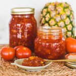 tomato jam in jars with pineapple and tomato in background.