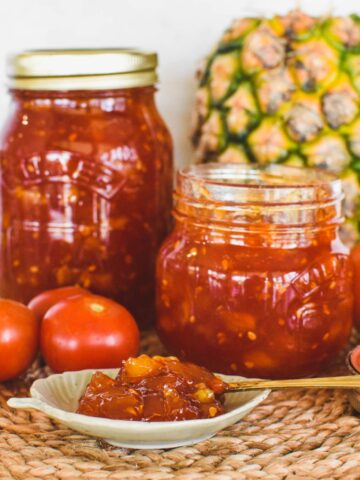 tomato jam in jars with pineapple and tomato in background.