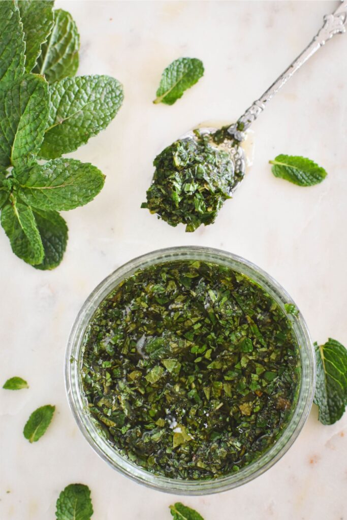 mint sauce in a container and on a spoon, surrounded by mint leaves.