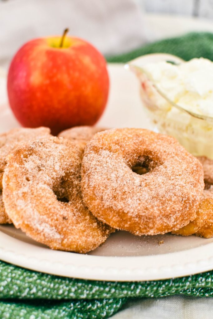 apple fritters served with cream and apple in background.