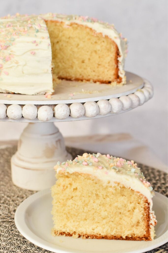 butter cake slice with whole cake in background on stand.