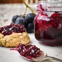 Grape jam in a jar, on a spoon and on a scone.