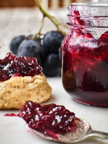 grape jam in jar, on spoon and on scone.