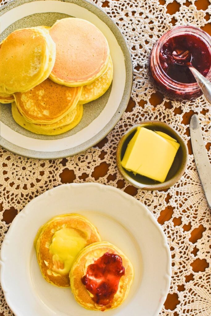 pikelets on table served with butter and jam.