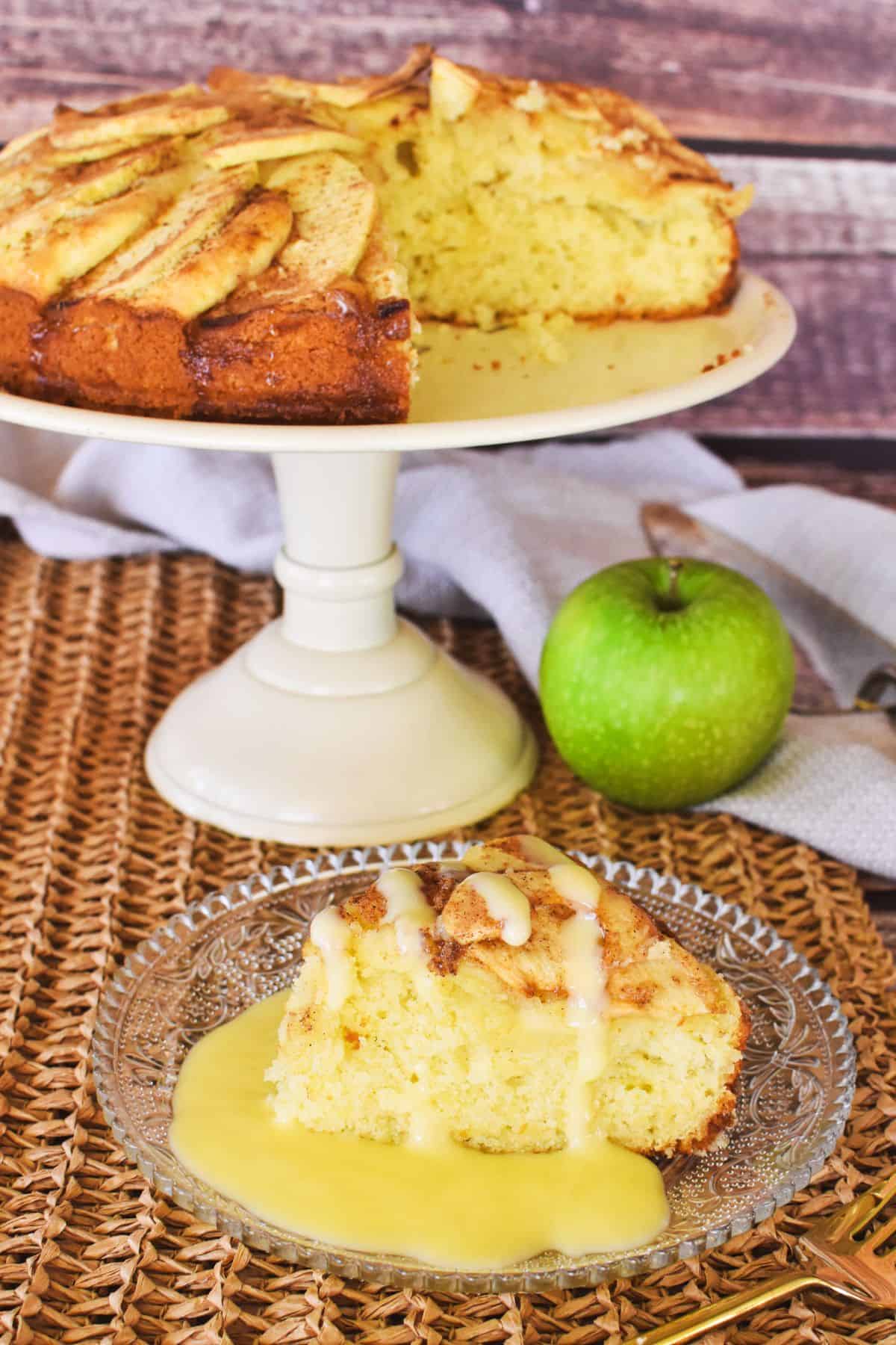 slice of apple tea cake with whole cake in background.