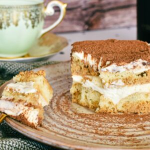 Slice of Tiramisu with Baileys served on a on plate with Green and Gold tea cup in background.