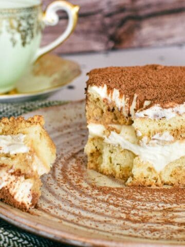 Slice of Tiramisu with Baileys served on a on plate with Green and Gold tea cup in background.