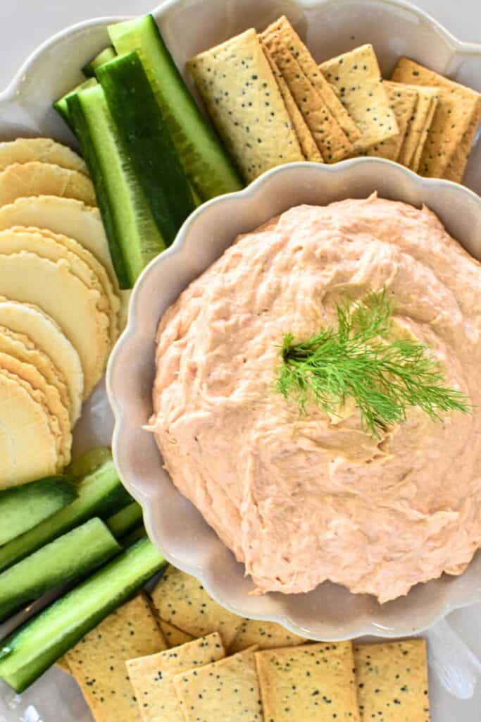 Salmon Dip surrounded by crackers and cucumber sticks.