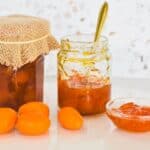 Kumquat Jam in jar with kumquats scattered on bench.