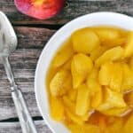 Stewed peaches in bowl on timber table with silver spoon at side.