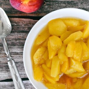 Stewed peaches in bowl on timber table with silver spoon at side.