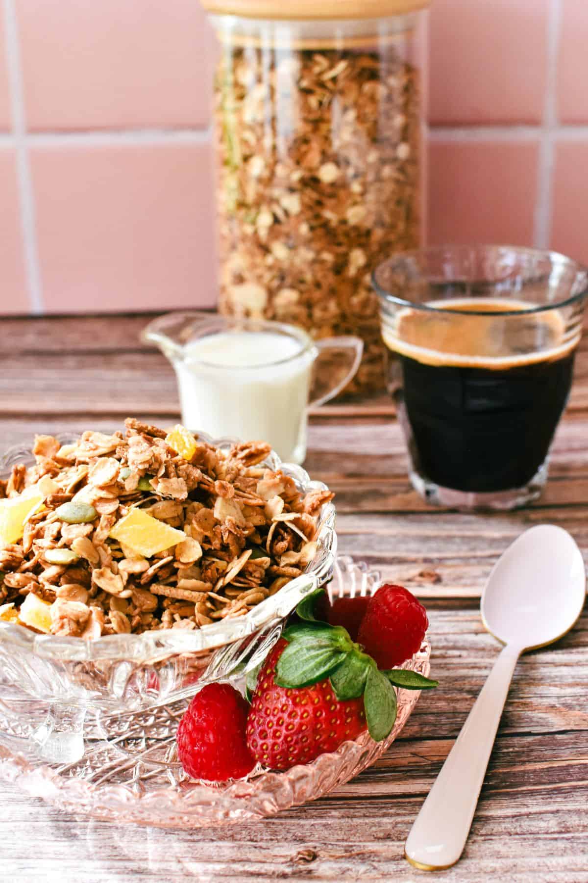 Toasted Muesli in bowl with fruit in foreground and coffee and milk in background.