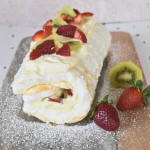 Pavlova Roll decorated with cream and fruit on serving board.