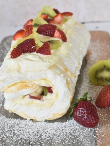 Pavlova Roll decorated with cream and fruit on serving board.